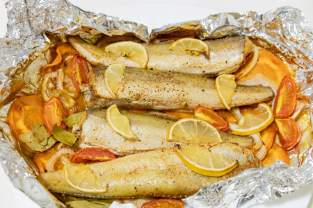 Spiced hake baked in the oven with lemon, tomatoes, carrots, and onions in foil. Delicious fish for...