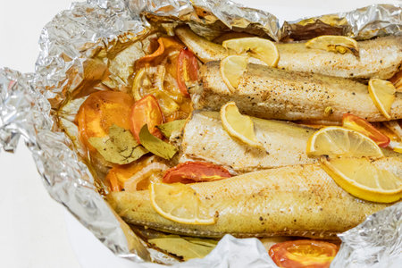 Spiced hake baked in the oven with lemon, tomatoes, carrots, and onions in foil. Delicious fish for...
