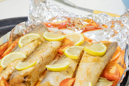 Prerape raw spiced hake for a bake in the oven with lemon, tomatoes, carrots, and onions in foil....