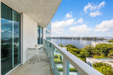 Beautiful view from the balcony towards the bay of Miami, bridge with trees, horizon, blue sky, tropical vegetation, table with chairs, glass railing with turquoise tintsの写真素材