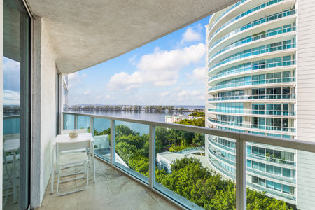 Beautiful view from the balcony towards the bay of Miami, bridge with trees, horizon, blue sky, tropical vegetation, table with chairs, glass railing with turquoise tintsの写真素材