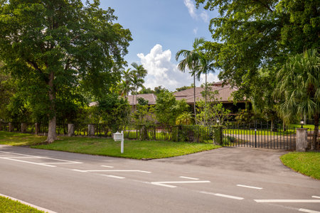 Facade of elegant house in luxury neighborhood of miami coral gables, view of the entrance gate street, trees, tiled roof, palms and blue sky with cloudsの写真素材