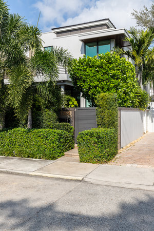 Facade of modern and elegant house, with abundant vegetation in front, door, sidewalk and blue sky streetの写真素材