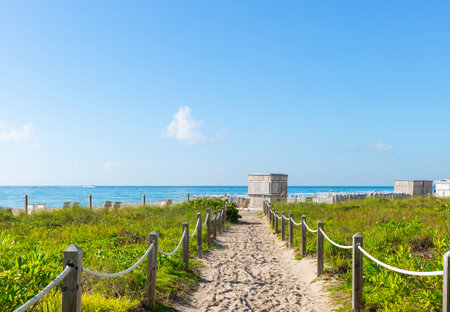 Beautiful entrance to the sea sand path with stakes with ropes, bushes and grass, beach, turquoise sea, blue skyの写真素材