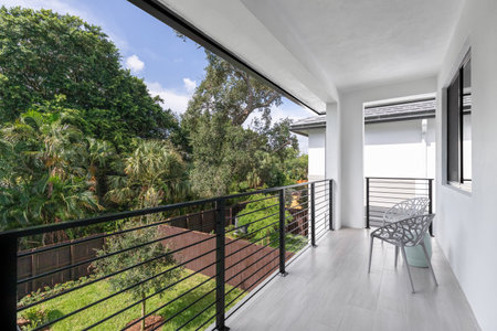 View from balcony of fenced backyard with wooden fences, short grass and tree in the middle, tropical vegetation around, outdoor chairs in gallery, in the Tarpon River neighborhoodの写真素材