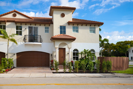 Facade of elegant cream colored colonial style house, sidewalk, short grass, driveway, street, balconies and blue sky in Croissant Park neighborhood of Fort Lauderdaleの写真素材