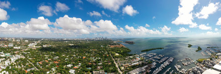Aerial drone shot of Grovenor House Coconut Grove in Miami, abundant tropical vegetation around, modern buildings and towers, blue sky with clouds and city in the backgroundの写真素材