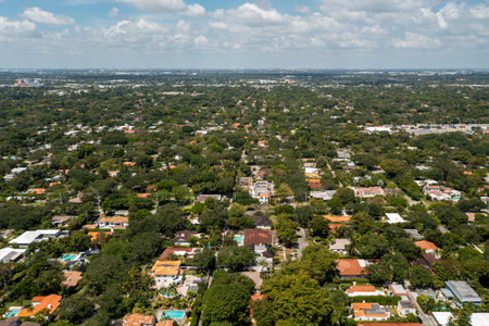 Aerial drone shot of suburb in Miami Shore village, Miami Dade County, with large tropical vegetation around, modern houses with elegance and style, summer weather, blue skyの写真素材