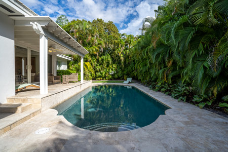 Beautiful backyard with concrete floor and pool, surrounded by tropical plants, porch with sun loungers, outdoor furniture, vines, located in Coral Gablesの写真素材