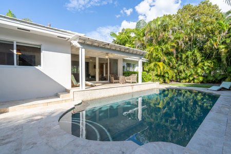 Beautiful backyard with concrete floor and pool, surrounded by tropical plants, porch with sun loungers, outdoor furniture, vines, located in Coral Gablesの写真素材