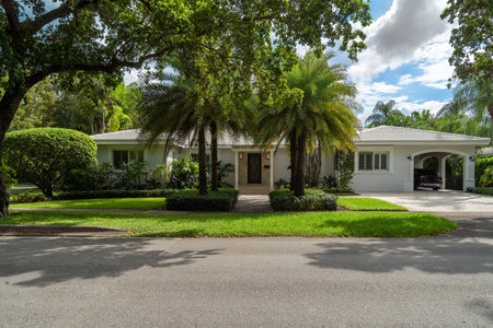 facade of a modern and luxurious colonial-style house in the city of Coral Gables, Miami-Dade, USA, with large tropical vegetation around it, open garage, main entrance, sidewalk,の写真素材