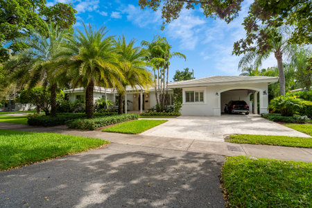 facade of a modern and luxurious colonial-style house in the city of Coral Gables, Miami-Dade, USA, with large tropical vegetation around it, open garage, main entrance, sidewalk,の写真素材