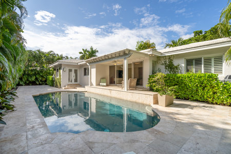 Beautiful backyard with concrete floor and pool, surrounded by tropical plants, porch with sun loungers, outdoor furniture, vines, located in Coral Gablesの写真素材