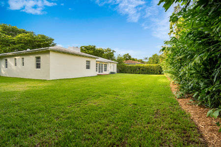 Beautiful backyard of modern and elegant house in the Golden Triangle neighborhood in the city of Coral Gables, short grass, tropical vegetation around, blue skyの写真素材