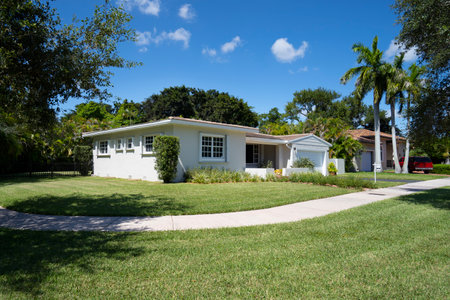 Facade of a modern and luxurious colonial-style house in the city of Coral Gables, Miami-Dade, USA, with large tropical vegetation around it, open garage, main entrance, sidewalk,の写真素材