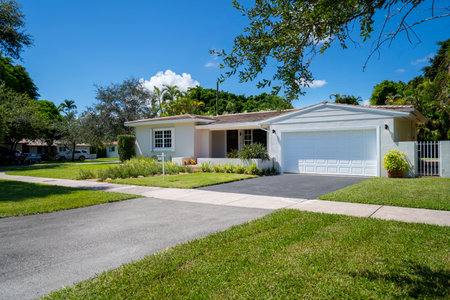 Facade of a modern and luxurious colonial-style house in the city of Coral Gables, Miami-Dade, USA, with large tropical vegetation around it, open garage, main entrance, sidewalk,の写真素材