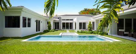 Backyard of elegant and modern house, located in Glenvar Heights, in Miami-Dade, white walls, black tiles, glass doors, short cepes, T-shaped pool, trees and palm trees around, sunの写真素材
