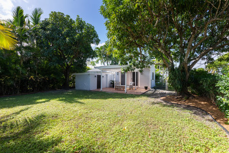 Beautiful patio with a wooden shed, with armchairs and an outdoor table in the West Flagler neighborhood, in Little Havana, short grass, privet walls, trees and palm trees, light bの写真素材