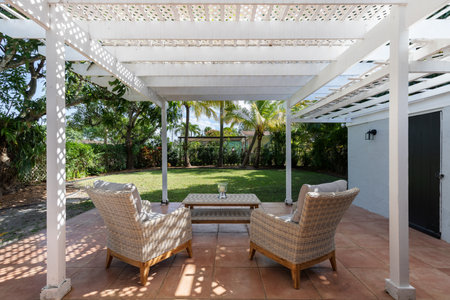 Beautiful patio with a wooden shed, with armchairs and an outdoor table in the West Flagler neighborhood, in Little Havana, short grass, privet walls, trees and palm trees, light bの写真素材