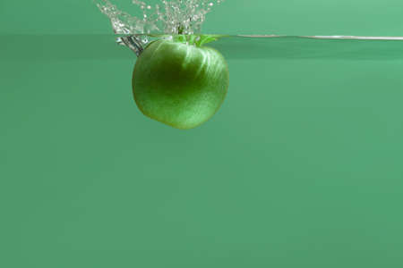 green apple falls into an aquarium with water on a green backgroundの写真素材