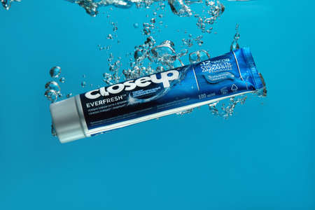 Russia, Samara - February 16, 2020 year. Closeup toothpaste in blue packaging drops in an aquarium with water on a blue backgroundのeditorial素材