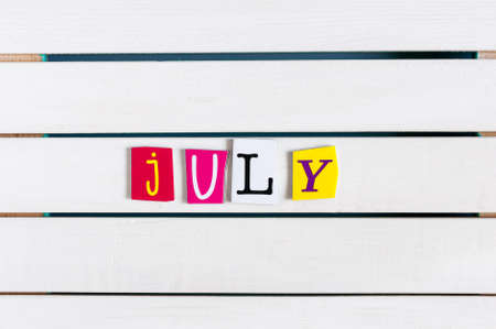 July written with color magazine letter clippings on white wooden board. Summer vacation concept.の写真素材