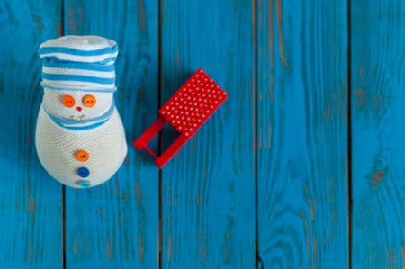 Red sled and handmade snowman on blue wooden background. Xmas card with empty space for text. Unique perspective, top view.の写真素材