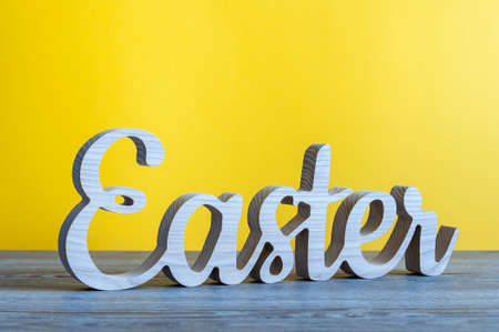 Easter - word carved of wood at yellow background. Holiday conceptの写真素材
