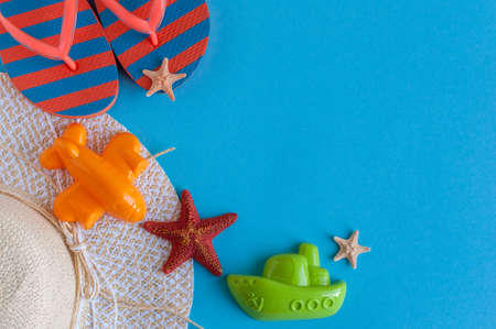 Flip-flops, beach panama hat, starfish and figure of ship and airplane on blue background. Traveler outfit, sea accessories. Summer vacation concept. Empty space for textの写真素材
