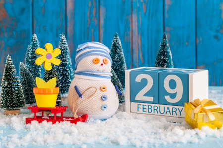 February 29th. Cube calendar for february 29 on wooden surface with snowman, sled, snow, fir and spring flower. Leap year, intercalary dayの写真素材