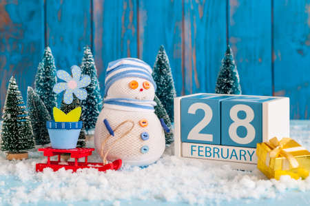 February 28th. Cube calendar for february 28 on wooden surface with snowman, sled, snow, fir and spring flowerの写真素材