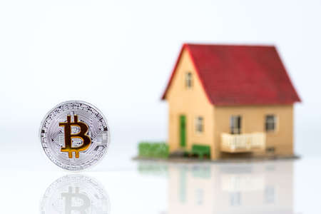 Bitcoin and private house model at light background. Real estate theme. Concept of Buying a property for crypto currencyの写真素材
