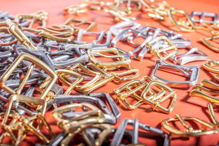 A lot of metal buckles for belts on red genuine full grain leather. Leather workshopの写真素材