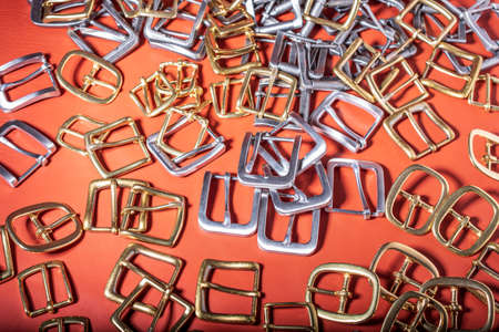 A lot of metal buckles for belts on red genuine full grain leather. Leather workshop