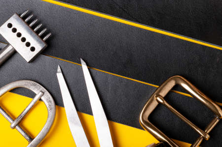 Belt buckles with leather tools on black full grain leather background. Materials, accessories on craftmans work deskの写真素材