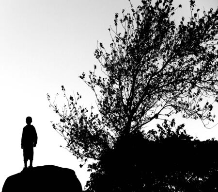 silhouette of boy stand on rock and tree, monotone colorの写真素材