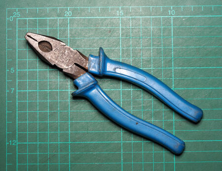 Old used plier on green cutting plate