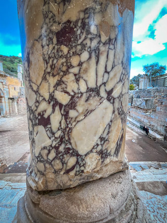 Intricate veined breccia marble patterns climb the fluted shaft of a towering column from the...