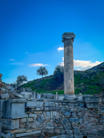 Fluted marble column topped by ornate acanthus capital stands isolated against scattered stone...