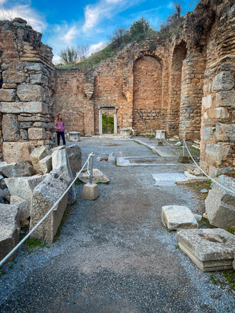 Scattered stone slabs line a gravel path flanked by tall weathered brick arches in the Trajan Temple...