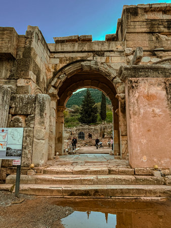 Tourists walk through the weathered Roman archway in ancient Ephesus, framing cypress-dotted hills...