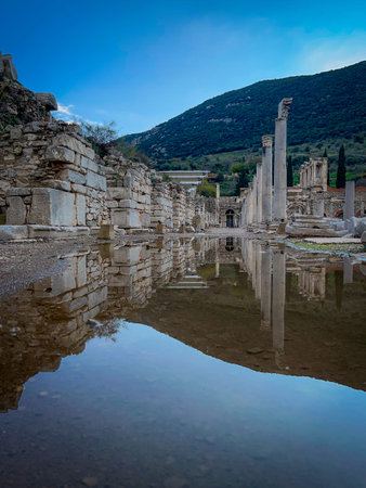 Shallow pools on the ancient stone pavement mirror towering columns and ruined arches of Ephesus'...