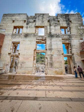 Modern visitors cross the rain-kissed striped marble forecourt toward the towering Library of Celsus...