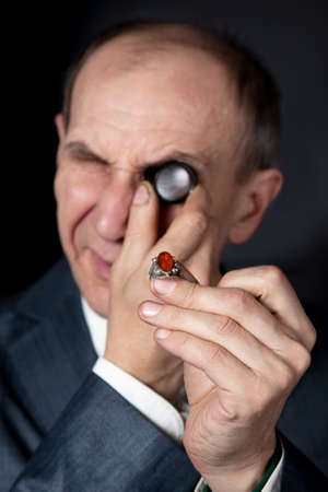 Old man appraising quality of ring with stone at black backgroundの写真素材