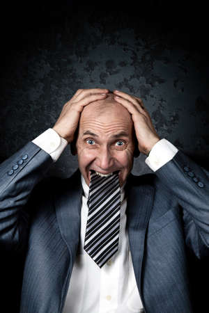 Businessman with Necktie in his mouth holding his head with hands on grunge backgroundの写真素材