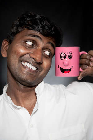 Handsome Indian man with funny mug smiling and looking at it close-upの写真素材