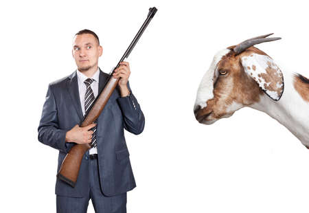Businessman with gun looking at big goat at white backgroundの写真素材