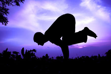 Man silhouette doing bakasana, crane pose with tree nearby outdoors at sun rise backgroundの写真素材