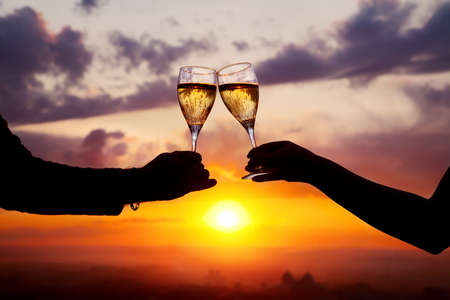 Man and woman clanging wine glasses with champagne at sunset dramatic sky backgroundの写真素材
