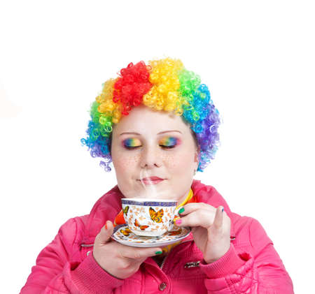 Beautiful woman in rainbow clown wig and creative rainbow make-up holding cup of tea and breathing in the steam at white background. Free space for textの写真素材